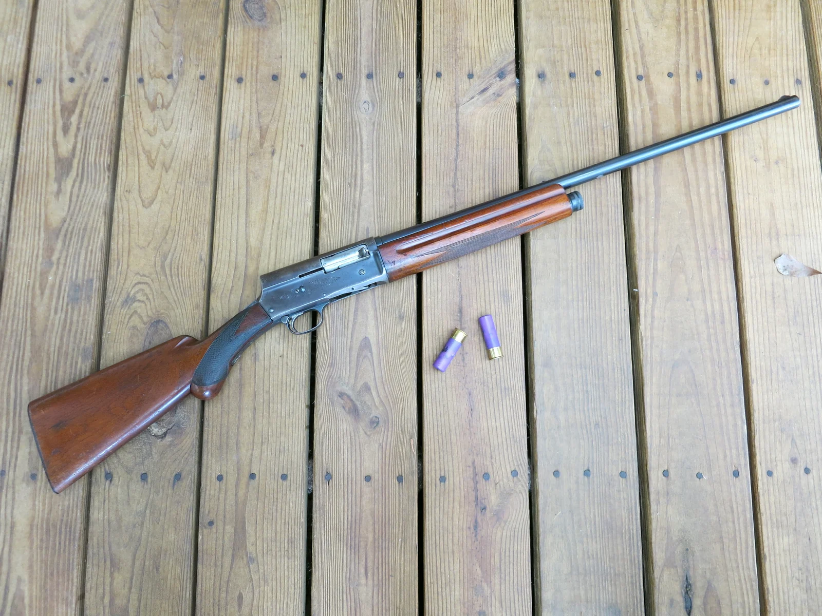 Worn Browning Auto-5 resting diagonally on wooden decking, with two loose shells nearby.